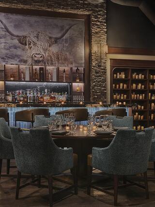 A cozy dining area features elegant decor, a well-stocked bar, and a striking highland cow portrait, creating a warm atmosphere.