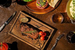 A beautifully plated steak on a wooden board, garnished with cherry tomatoes and rosemary, surrounded by elegant dining elements.
