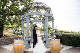 A couple embraces under a beautiful gazebo surrounded by vineyards, creating a romantic and picturesque wedding scene.
