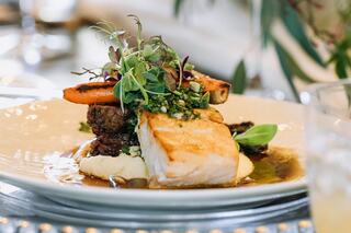 A beautifully plated dish features a seared fish fillet atop creamy mashed potatoes, garnished with fresh herbs and vibrant vegetables.