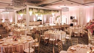 An elegant banquet hall featuring gold chairs, floral arrangements, soft lighting, and a beautifully decorated stage for celebrations.