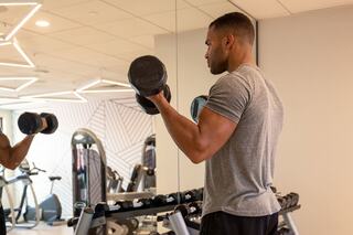 A man in a gym lifts dumbbells, showcasing determination as he focuses on his workout in a modern fitness space.