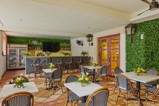 A quaint dining area features potted flowers on tables, a bar with beverages, and vibrant green walls, creating a cozy atmosphere.