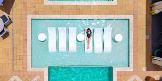 A person relaxes on floating loungers in a stylish pool, surrounded by calm water and vibrant tiles, enjoying a sunny day.