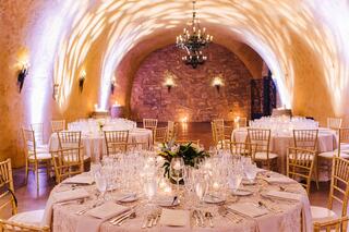 Elegant dining setting in a softly lit venue, featuring round tables adorned with white linens and crystal glassware, creating a romantic ambiance.