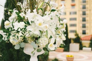 A lush arrangement of white flowers and greenery in a decorative vase, set against a backdrop of elegant architecture.