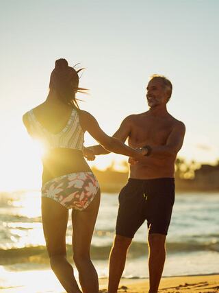 A couple dances joyfully on the beach at sunset, basking in the warmth and light, creating a moment of connection and happiness.