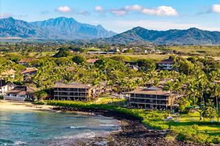 A coastal scene features lush greenery, palm trees, and charming buildings along the shore, with majestic mountains in the background.
