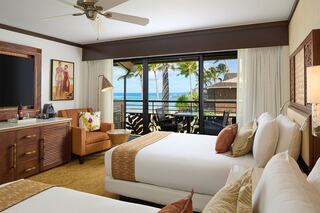 Brightly lit room featuring two beds, tropical decor, and a balcony with ocean views, creating a relaxing vacation atmosphere.