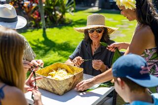 A joyful gathering of people crafting together outdoors, surrounded by lush greenery and vibrant flowers, sharing smiles and creativity.