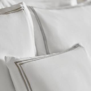 Soft, white bedding set featuring elegant grey trim on pillows, creating a serene and inviting atmosphere for rest and relaxation.