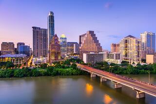 A vibrant skyline at dusk features modern skyscrapers and a bustling bridge, reflecting the lively atmosphere of a city by the water.