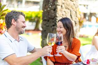 A man and woman toast with glasses of wine, sharing joyful smiles in a vibrant outdoor setting.