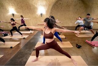 A woman is practicing yoga on a mat while following an online class displayed on a laptop.