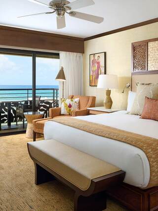 A stylish bedroom with a beach view, featuring a king-sized bed, cozy seating, and tropical decor. Bright and inviting atmosphere.
