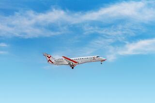 A sleek regional jet descends against a backdrop of clear blue skies and wispy clouds, showcasing its modern design and logo.