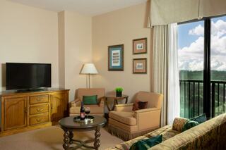A cozy hotel suite features a comfortable seating area, a TV, stylish decor, and large windows with a scenic view.
