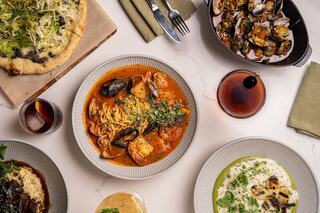 A delicious spread features pasta with seafood, a savory pizza, and creamy risotto, complemented by drinks in elegant settings.