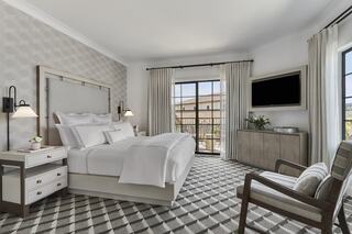 A stylish, modern luxury hotel bedroom with a king-sized bed, patterned rug, sleek furniture, large windows, and a cozy atmosphere.