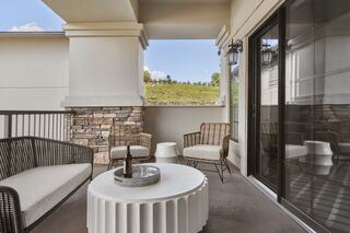 A cozy balcony features stylish seating and a round table, overlooking a scenic view of rolling green hills and a clear sky.