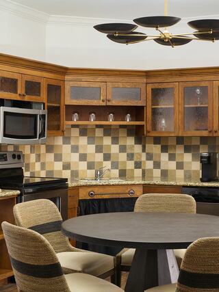 A stylish kitchen features wooden cabinetry, a patterned backsplash, modern appliances, and a circular dining table with woven chairs.