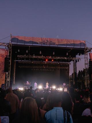 A bustling concert scene at dusk, with performers on stage and a crowd enjoying the vibrant atmosphere under the fading sky.