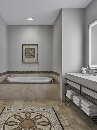 A stylish bathroom featuring a bathtub, modern double sink, elegant tile work, and a decorative wall piece, creating a serene atmosphere.