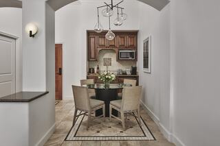 A cozy kitchen nook features a round table with four chairs, a stylish chandelier, and tasteful decor against a warm wooden backdrop.