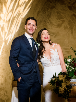 A happy couple stands close together, smiling joyfully. The woman wears an elegant lace gown, while the man is in a stylish suit, creating a romantic ambiance.