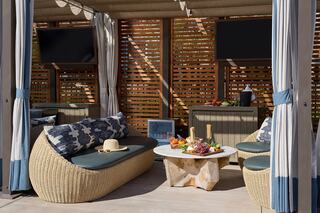 A cozy outdoor lounge features comfortable seating, a round table with fruit, and privacy curtains, creating a stylish relaxation space.
