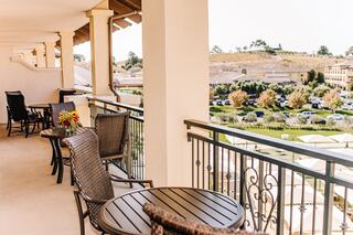 A spacious balcony with wicker chairs and tables overlooks a scenic view, adorned with potted flowers and nearby parked cars.