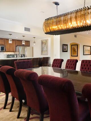 A stylish dining area features plush burgundy chairs around a sleek table, complemented by an elegant chandelier and a modern kitchen backdrop.