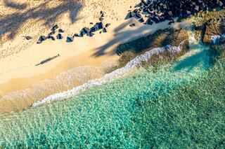 A pristine beach with golden sand and clear turquoise waters, bordered by rocks and gentle waves, under the warm sunlight.