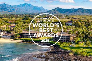 A coastal scene features beachfront resorts amid lush palm trees, with majestic mountains in the background under a bright blue sky.