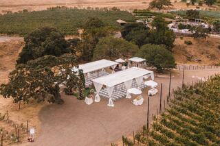 A beautiful outdoor wedding setup features a white canopy, chairs arranged for guests, and scenic vineyards in the background.