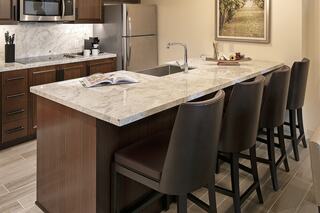 A modern kitchen features a marble-topped island with bar stools, sleek cabinetry, and stainless appliances in a warm, inviting setting.