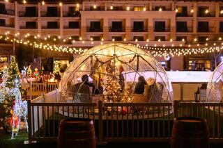 Cozy, illuminated igloos surrounded by festive decorations and twinkling lights create a charming winter atmosphere for gatherings.
