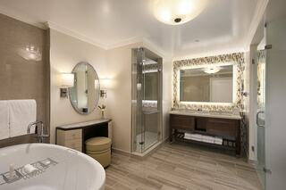 A modern bathroom features a freestanding tub, walk-in shower, elegant lighting, and a stylish vanity with a mirror. Warm, neutral tones dominate.