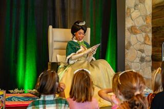 A princess in a green gown reads to captivated children seated in front of her, creating a magical storytelling moment.