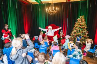 A festive scene with Santa Claus engaging joyfully with excited children in front of a decorated Christmas tree and vibrant backdrop.