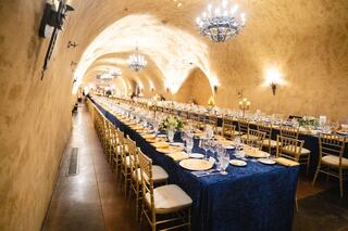 A beautifully arranged long dining table in an elegant, arched venue, adorned with chandeliers and luxurious table settings.