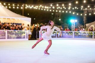 A skater performs gracefully on ice, surrounded by a festive crowd and twinkling lights, capturing the joy of winter celebrations.
