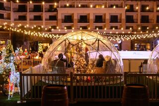 Brightly lit igloos with decorations and a Christmas tree create a festive atmosphere, surrounded by holiday lights and joyful decor.