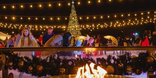 A cozy scene featuring decorated igloos, festive lights, and a Christmas tree, creating a warm holiday atmosphere outdoors.