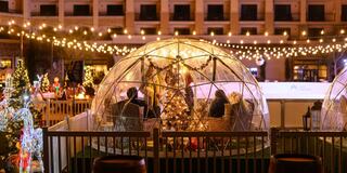 A cozy scene featuring decorated igloos, festive lights, and a Christmas tree, creating a warm holiday atmosphere outdoors.