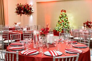 A festive dining setup features red tablecloths, striped napkins, floral centerpieces, and a beautifully decorated Christmas tree.