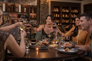 A joyful group of friends clinks glasses and shares laughter over an elegantly set dinner table, surrounded by warm lighting.