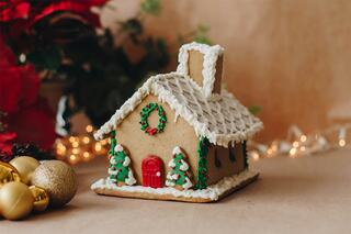 A decorated gingerbread house with a snowy roof, colorful icing, a red door, and small trees, set against a festive backdrop.