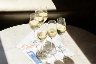 Six elegant glasses of sparkling wine sit on a marble table, accompanied by menus, illuminated by soft natural light.