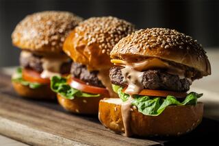 Three delicious cheeseburgers with sesame seed buns, lettuce, tomato, and a creamy sauce, beautifully arranged on a wooden platter.